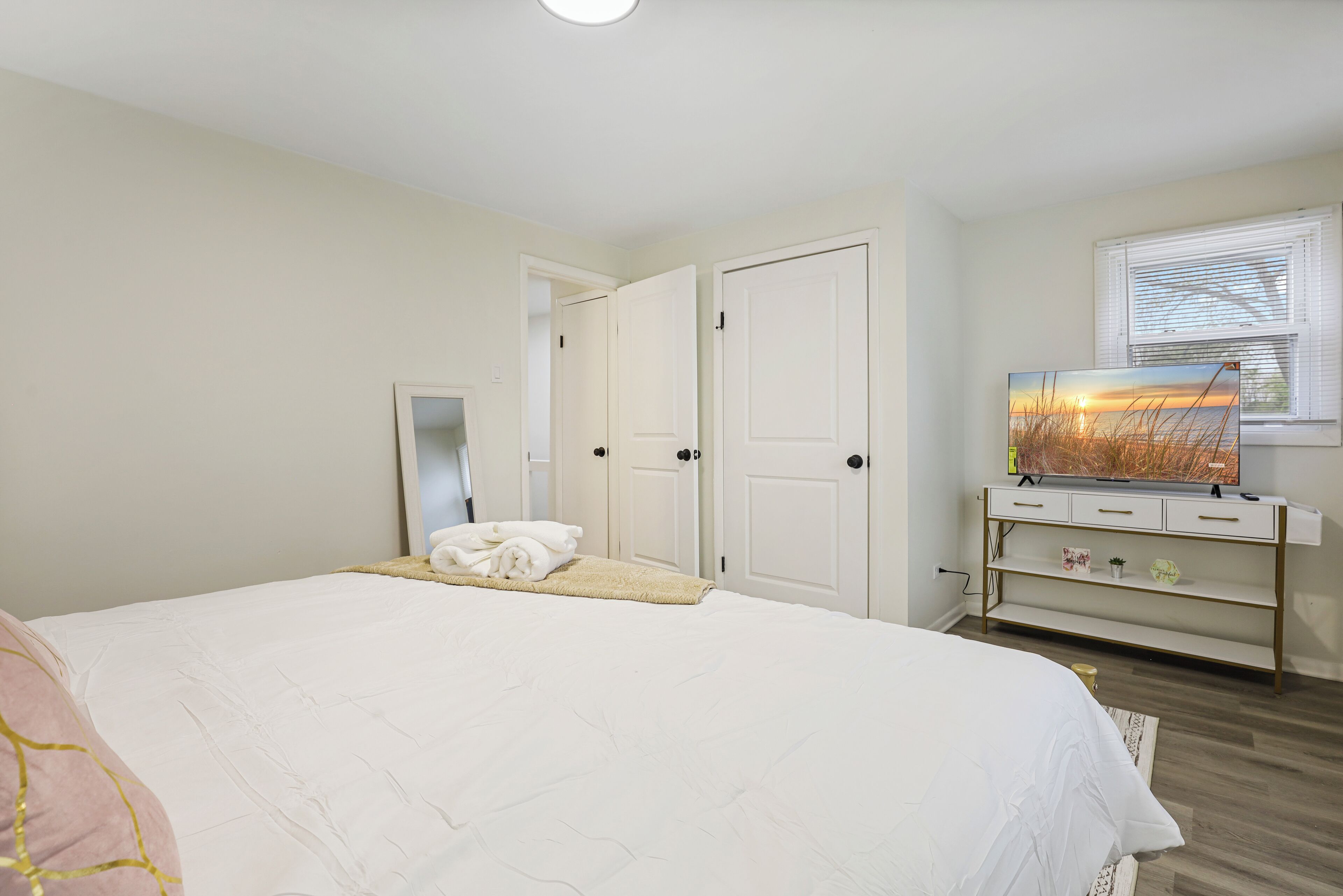 Une chambre avec un grand lit, une commode, un miroir et une fenêtre avec des stores.