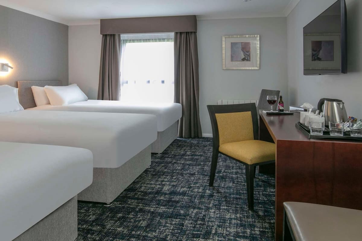Habitación de hotel con dos camas, un escritorio con silla, cafetera y ventana con cortinas.