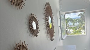 A room with a white wall adorned with wooden sunburst wall art, a white cabinet, and a window offering a view of greenery.