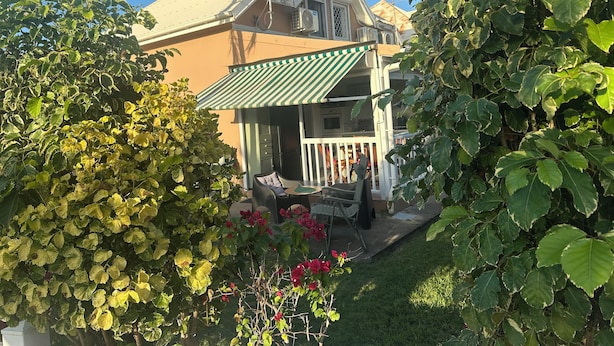 A house with a porch, surrounded by lush greenery and a clear blue sky.