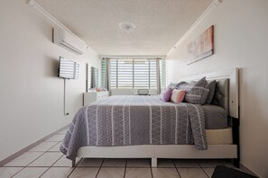 Un dormitorio con cama, mesita de noche, espejo y ventana con persianas.