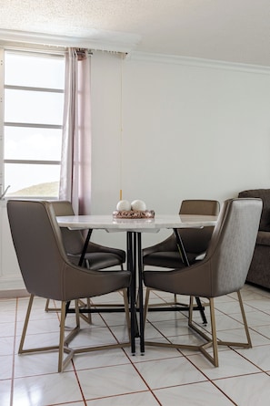 Un coin repas avec une table et quatre chaises, une fenêtre avec des rideaux et un canapé à l’arrière-plan.