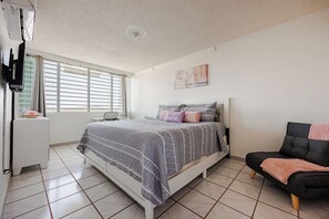 Quarto com cama, cadeira, escrivaninha e janela com persianas.