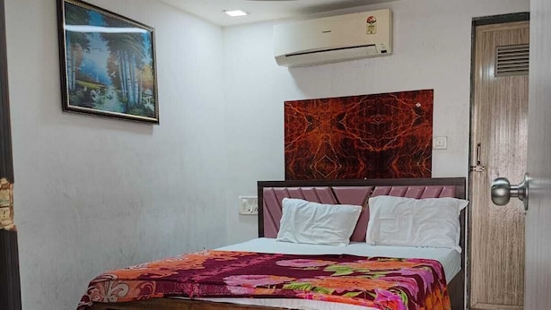 A bedroom with a bed, a ceiling fan, a wall-mounted air conditioner, and a door. - Hotel Sweet Dream (Rajkot)
