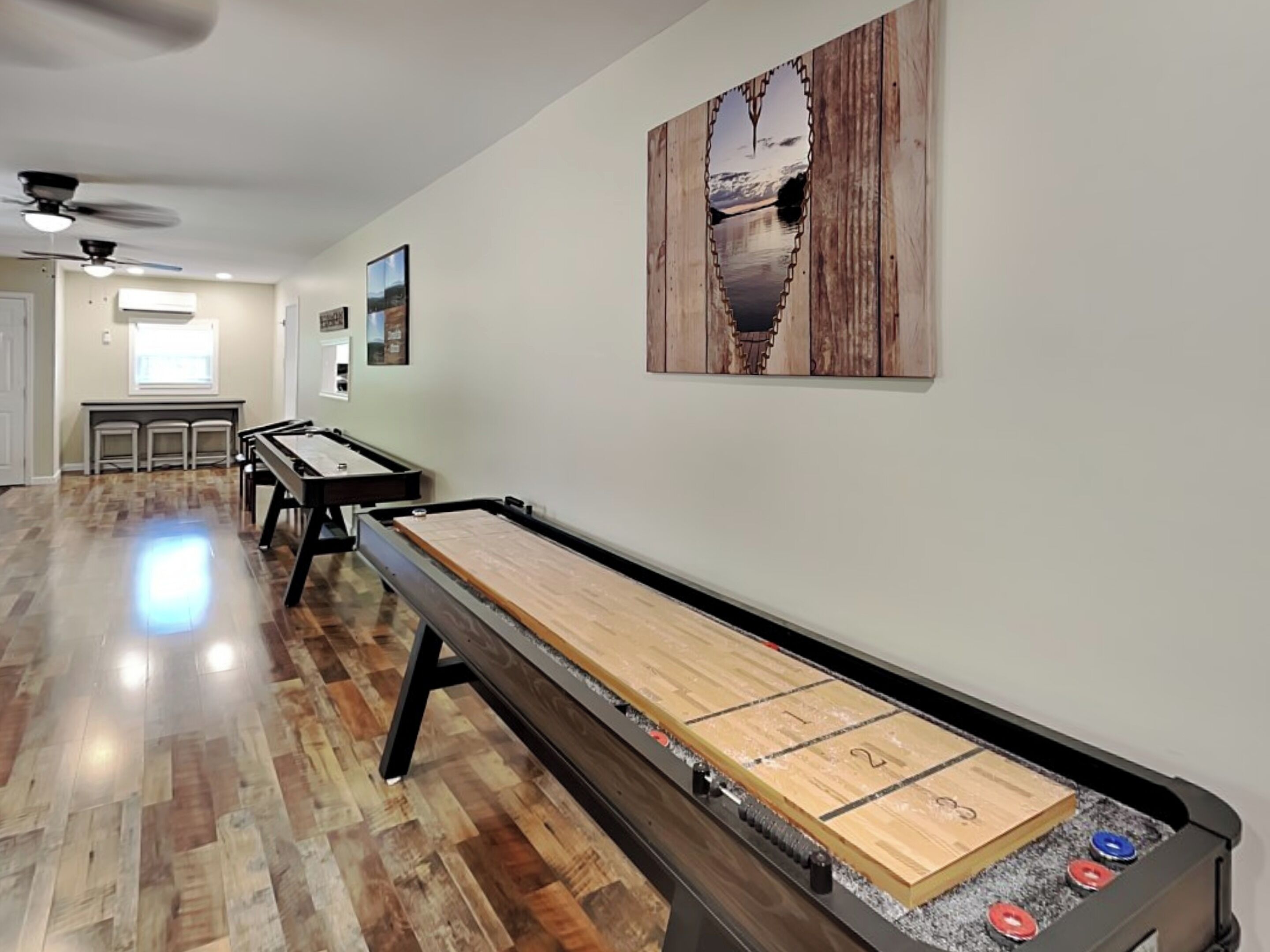 Une table de billard dans une pièce dotée d’un plancher en bois, d’un ventilateur de plafond et d’une œuvre d’art accrochée au mur.