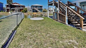 Un quartier résidentiel avec une pelouse verdoyante, un banc en bois, un petit étang et un escalier menant à une maison bleue.