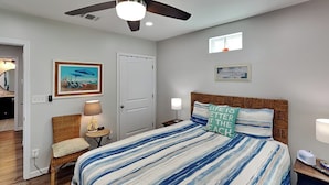 Une chambre à coucher comprenant un lit, une chaise, une table de chevet, une lampe, un tableau encadré et un ventilateur de plafond.