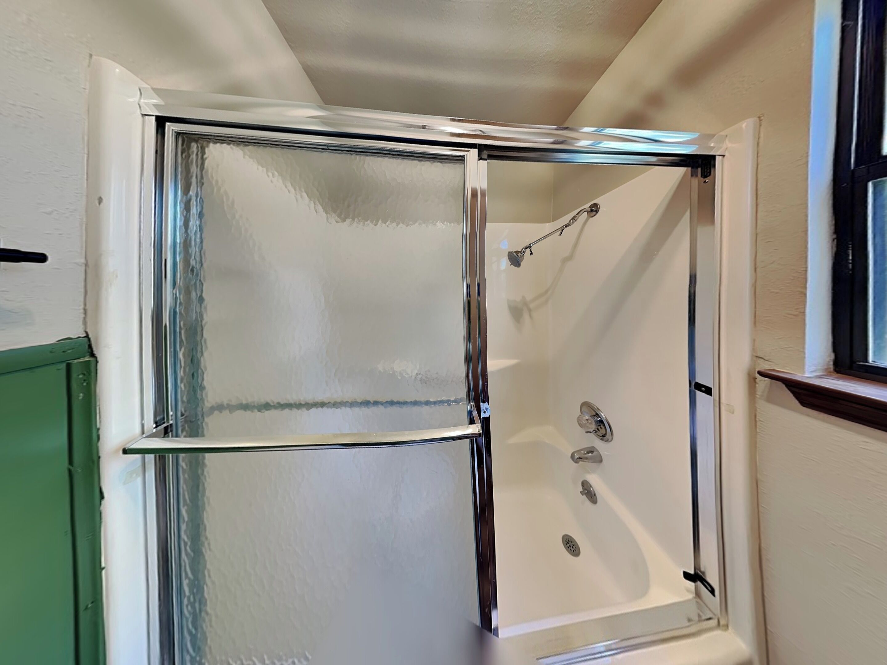 A shower with a glass door, a handheld showerhead, and a wall-mounted faucet.