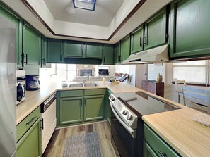 A compact kitchen with green cabinets, a built-in oven, and a microwave. - Fireside Cabin (Ruidoso)