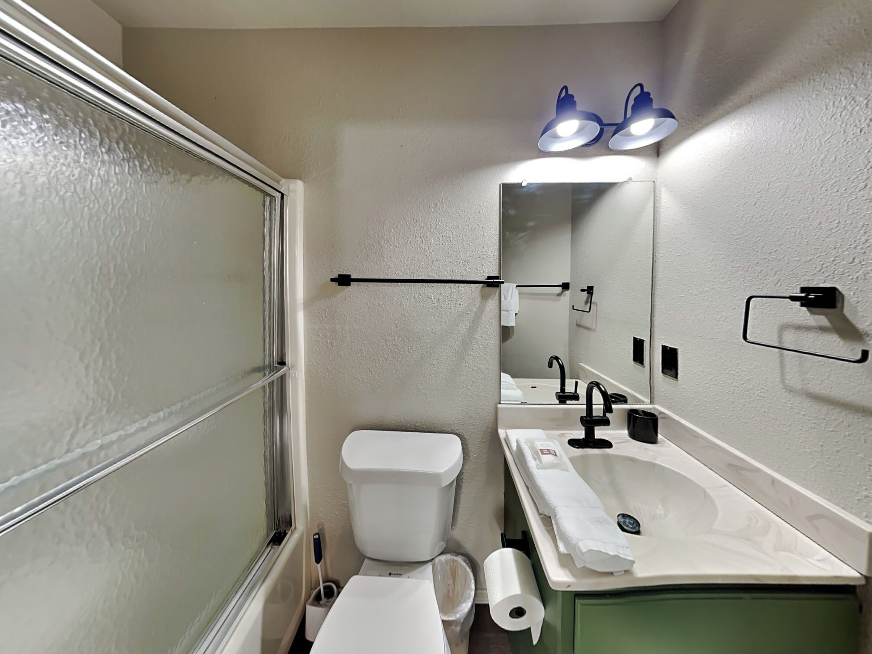 A bathroom with a toilet, sink, mirror, towel rack, and a towel dispenser.
