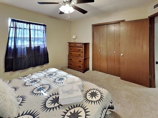 A bedroom with a bed, a dresser, a wardrobe, a ceiling fan, and a window with curtains. - Fireside Cabin (Ruidoso)