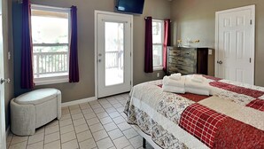 Een slaapkamer met een bed, een plafondventilator, een televisie, een dressoir en een raam met gordijnen.