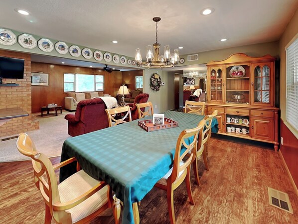 A dining area with a table set for four, surrounded by wooden chairs. A chandelier hangs from the ceiling, and there is a wooden cabinet with glass doors to the right. - Brooksland (Ruidoso)