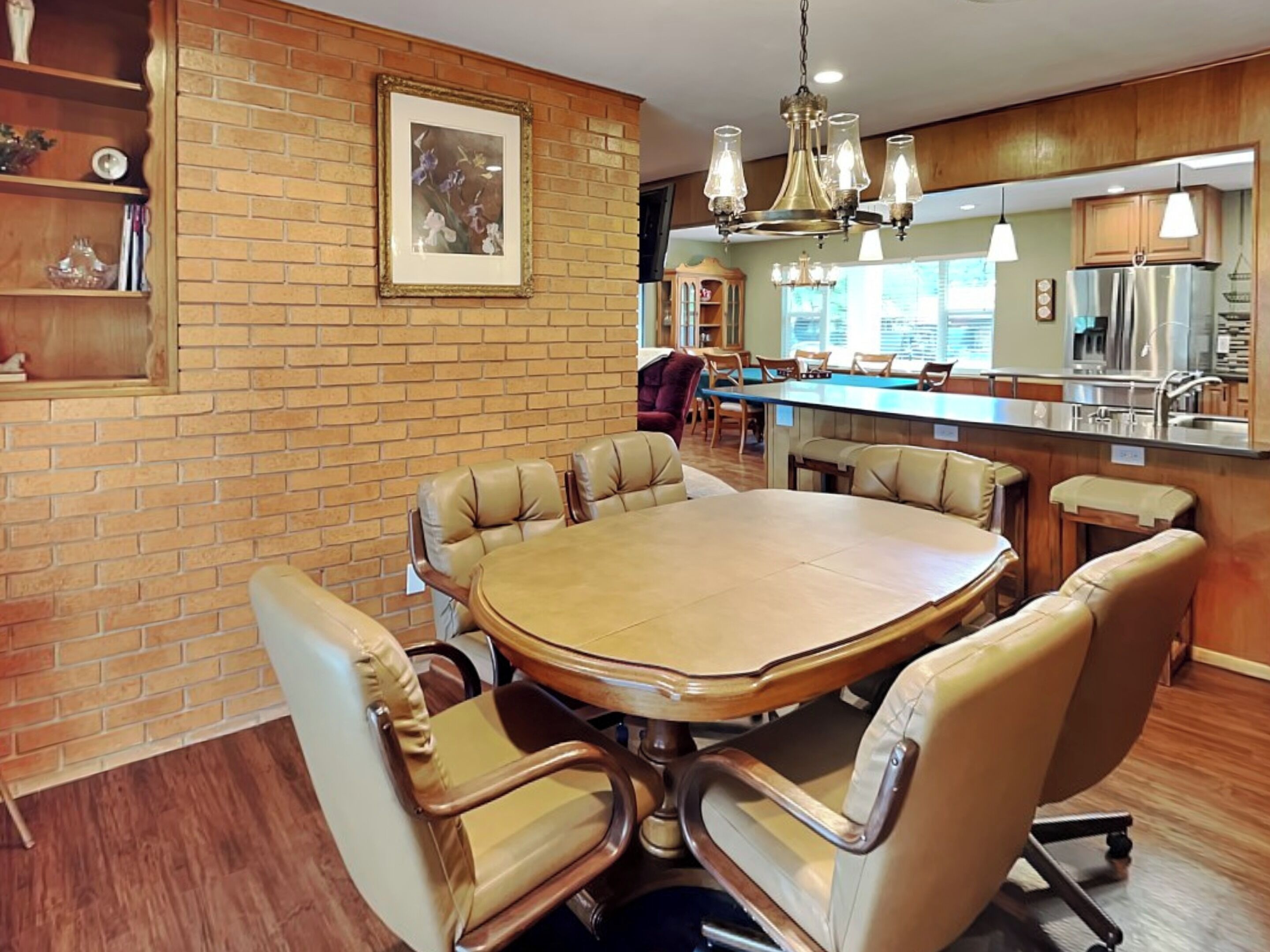 A dining area with a large oval table surrounded by leather chairs, a brick wall, and a chandelier.