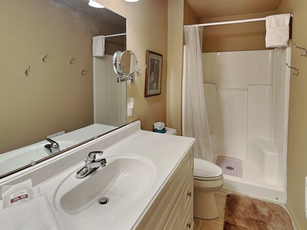 A bathroom with a white sink, mirror, toilet, and shower. - Brooksland (Ruidoso)