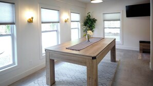 A spacious room with a wooden dining table, large windows, and a flat-screen TV mounted on the wall.