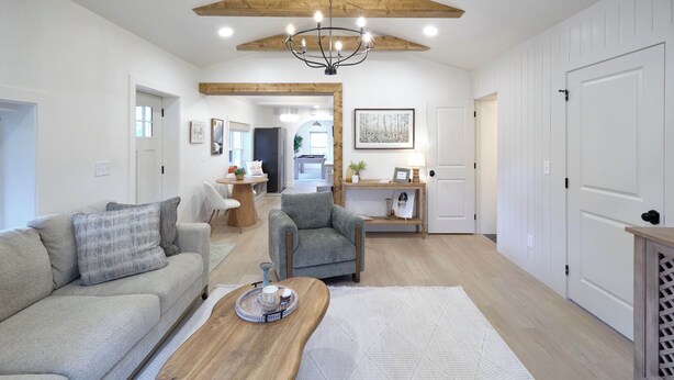 A spacious living room with a sofa, armchair, wooden coffee table, and a chandelier.