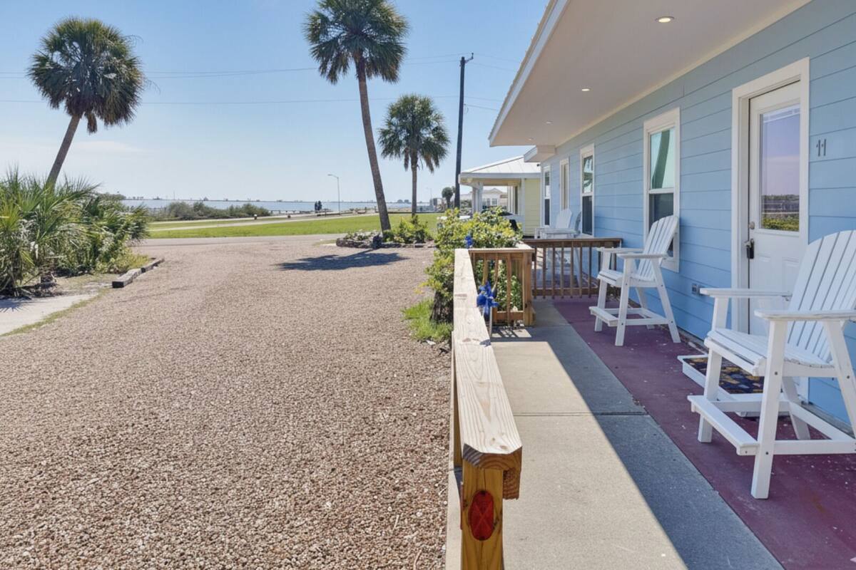 A beachfront property with a gravel driveway leading to a porch with white Adirondack chairs.