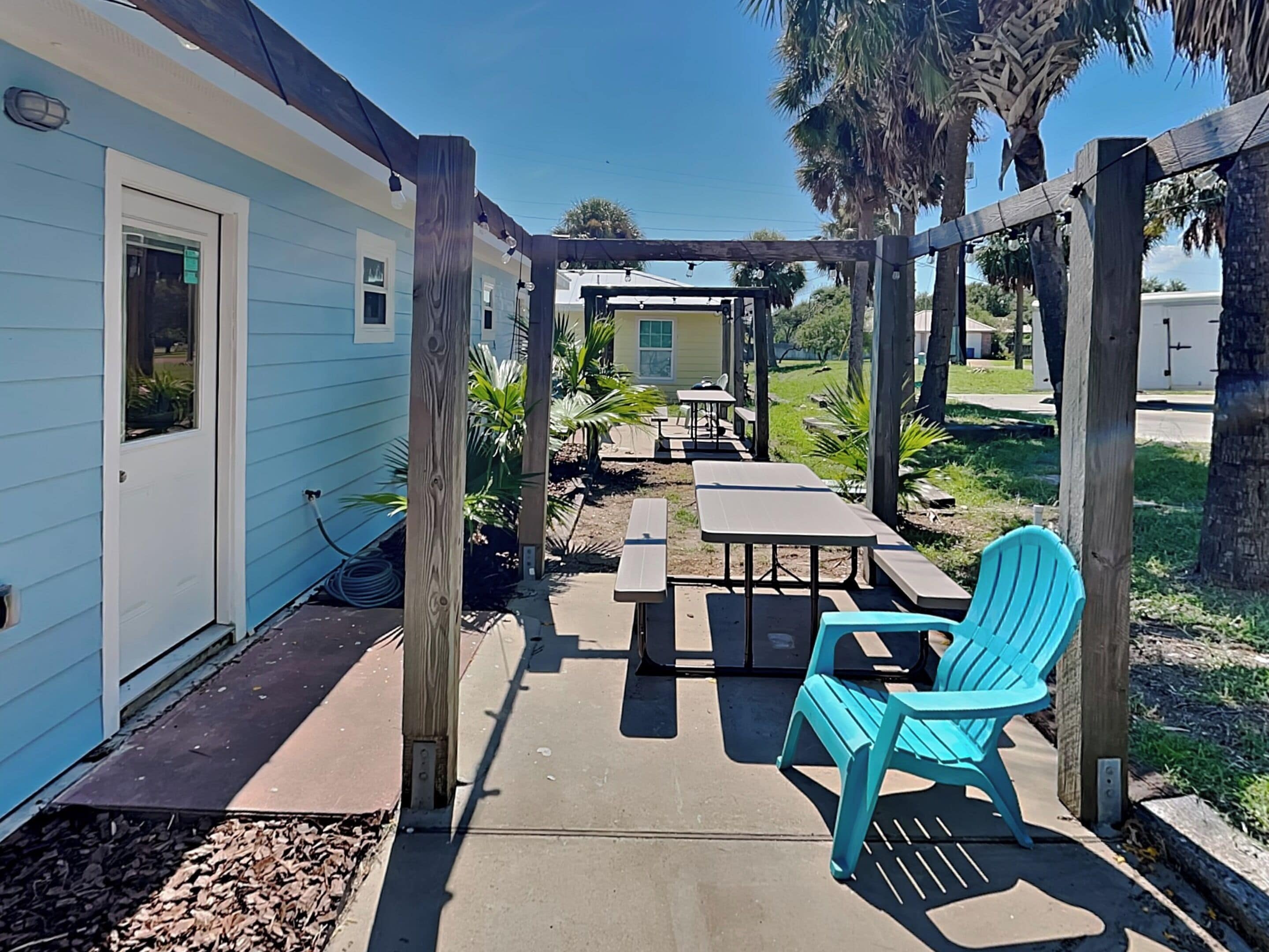 A patio area with a wooden pergola, picnic tables, and a turquoise Adirondack chair.