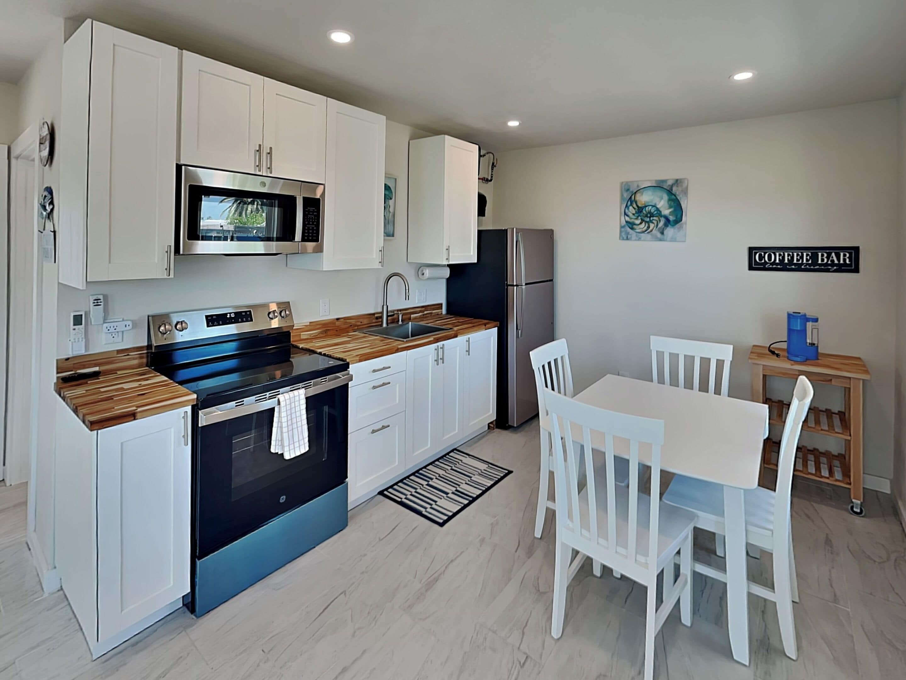 A modern kitchen with white cabinets, a stainless steel refrigerator, a microwave, and a coffee bar sign.