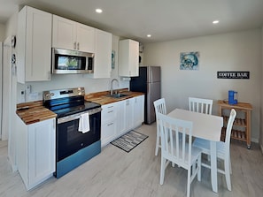 A modern kitchen with white cabinets, a stainless steel refrigerator, a microwave, and a coffee bar sign.