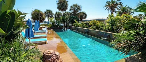 Una piscina con agua cristalina, rodeada de palmeras y sombrillas azules.