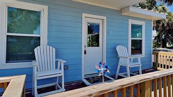 A house with blue siding and white trim, featuring two white Adirondack chairs and a small garden area with a decorative pinwheel.