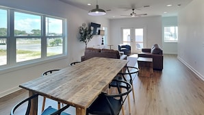 Un vaste espace de vie comprenant une table à manger en bois, des chaises noires, un canapé et un ventilateur de plafond.