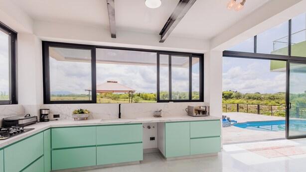 A modern kitchen with green cabinets, a large window, and a view of a swimming pool.