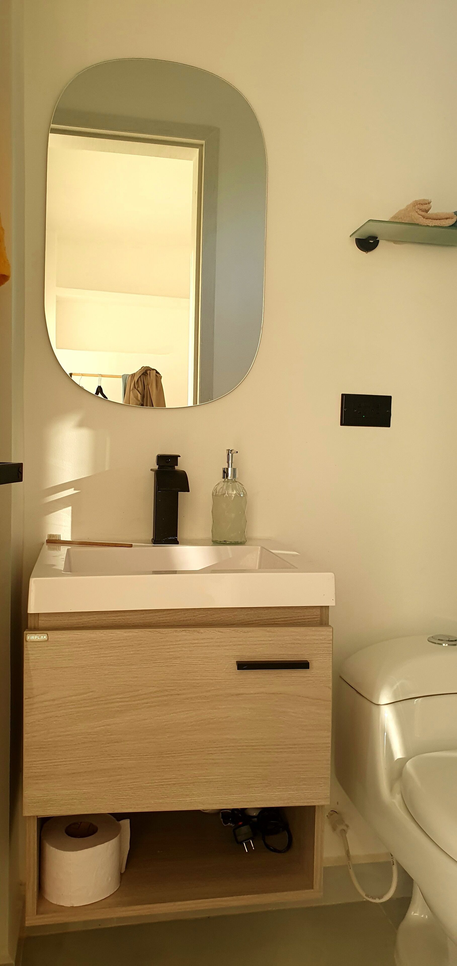 Ein Badezimmer mit weißem Waschbecken, einem Spiegel, einem Handtuchhalter und einer Toilette.