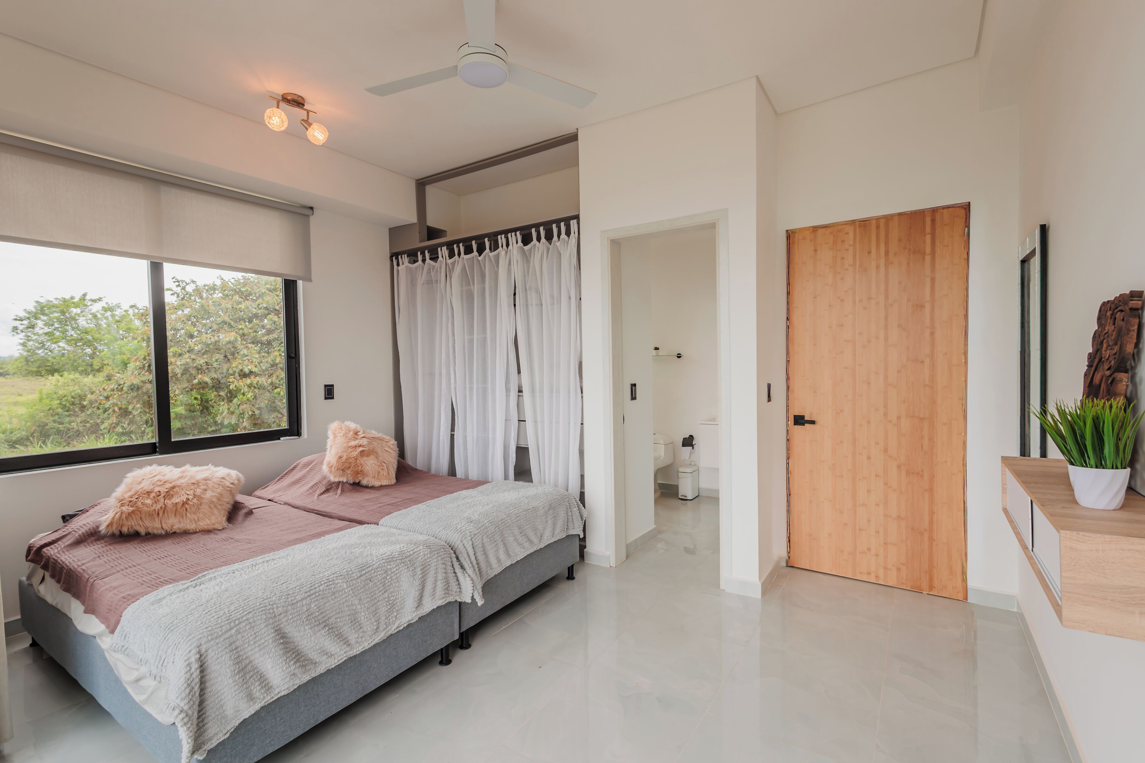Camera moderna con un grande letto, una ventola a soffitto e vista sull'esterno attraverso una finestra.