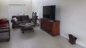 Un salón con un sofá de cuero marrón, una mesita de centro, un televisor sobre un mueble de madera y una puerta al fondo.