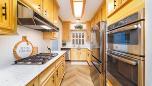 Een keuken met houten kasten, roestvrijstalen apparatuur en een visgraatvloer.
