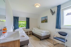 A room with a bed, a desk, a chair, a window with curtains, a painting, and a sink. - Charming Villa With Sauna and South-facing Garden (De Koog)