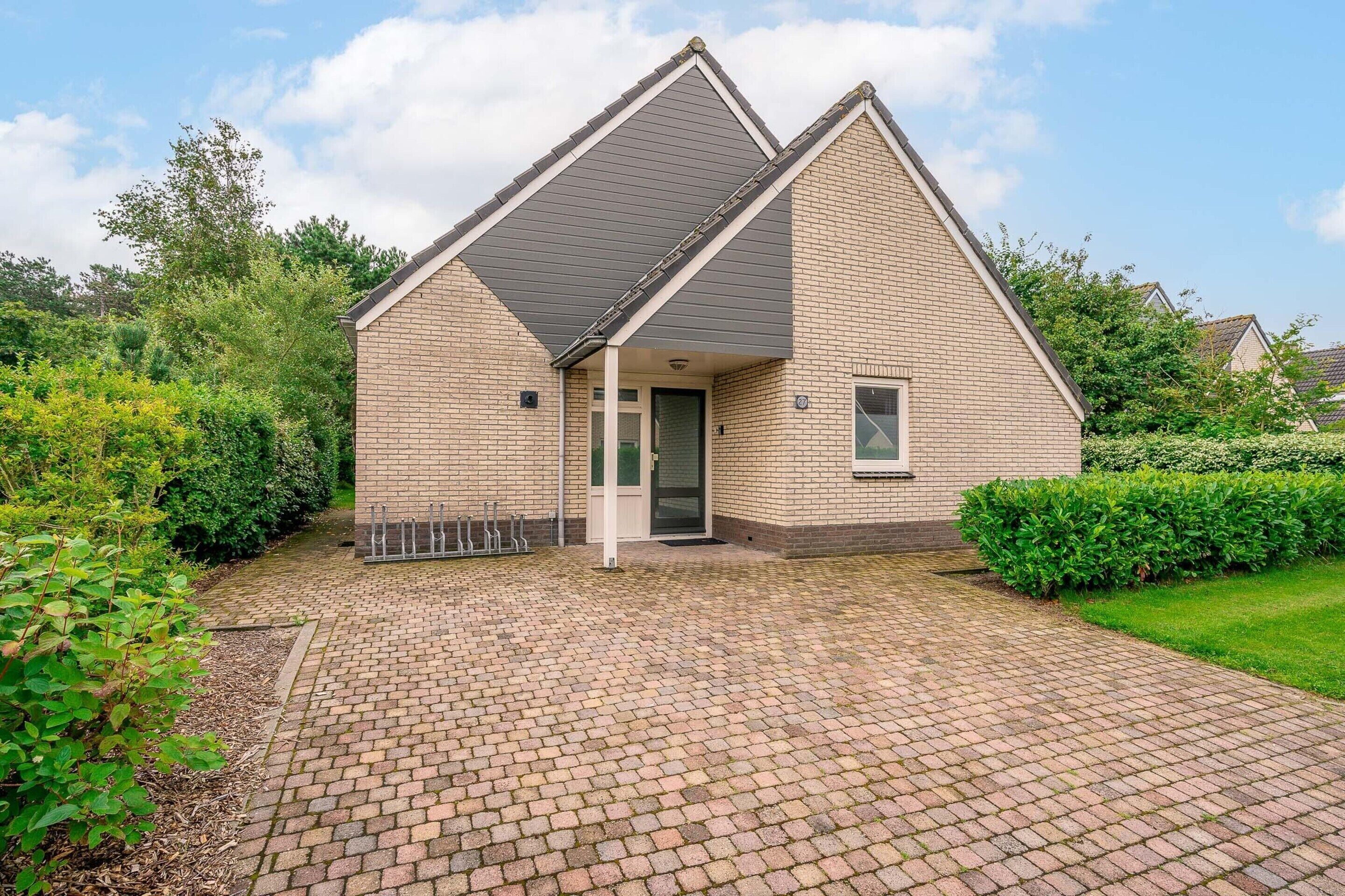 A two-story house with a brick exterior, a sloped roof, and a paved driveway.