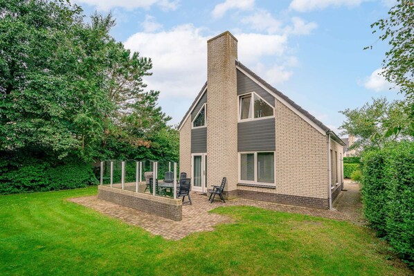 A modern two-story house with a brick exterior, a chimney, and a covered patio with outdoor furniture. - Charming Villa With Sauna and South-facing Garden (De Koog)