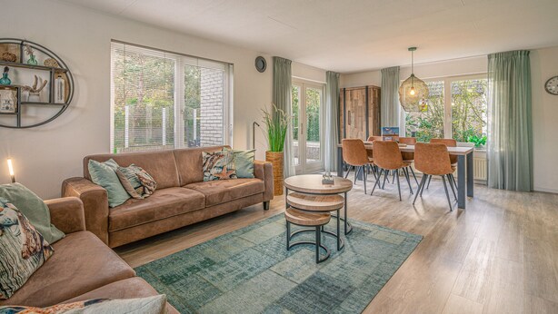Ein modernes Wohnzimmer mit einem braunen Sofa, einem Esstisch mit Stühlen und einem großen Fenster mit Jalousien.