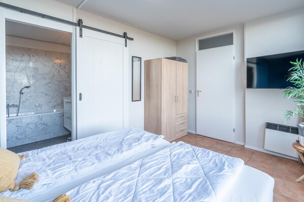 A bedroom with a bed, a wardrobe, a television, and a bathroom with a shower.