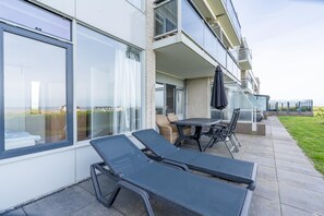 Ein moderner Außenbereich mit Lounge-Möbeln und Tisch, mit Blick auf eine Rasenfläche.