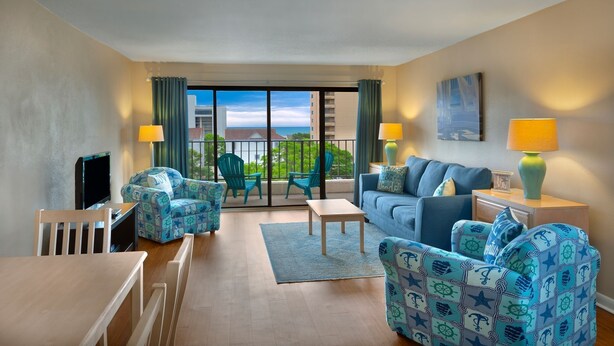 A hotel room with a balcony, a sofa, a chair, a TV, and a lamp. - 2BR Condo in Myrtle Beach w/ Kitchen + Pool Access (Myrtle Beach)