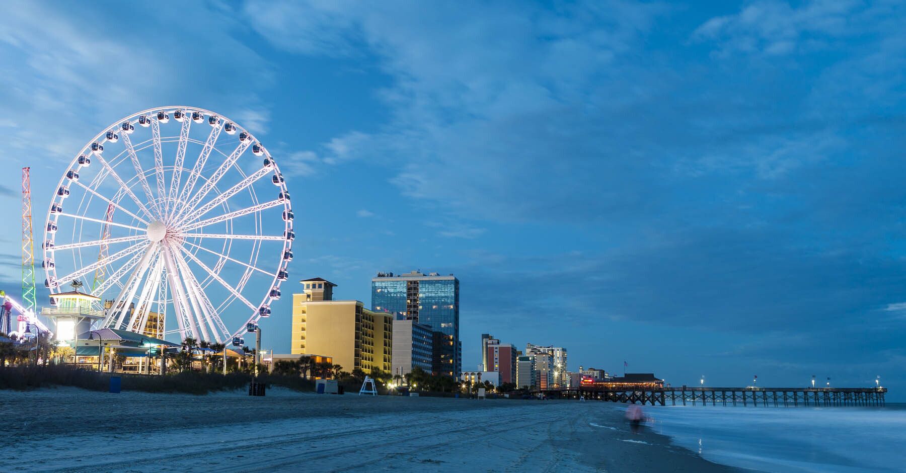 Ein Strand mit einem großen Riesenrad, einer Promenade und modernen Gebäuden im Hintergrund.
