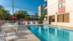 A swimming pool with lounge chairs and umbrellas, surrounded by a building with a red and beige facade. - 2BR Condo in Myrtle Beach w/ Kitchen + Pool Access (Myrtle Beach)