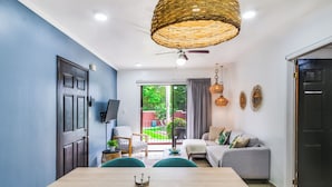 A modern living room with a dining table, sofa, and a large window with a view of greenery.