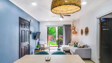 A modern living room with a dining table, sofa, and a large window with a view of greenery.