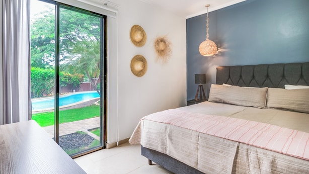 A bedroom with a large bed, a view of a swimming pool, and a sliding glass door.