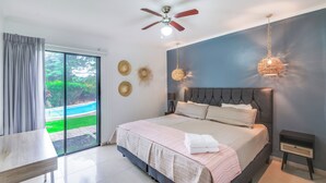 A modern bedroom with a large bed, a ceiling fan, and a view of a swimming pool.