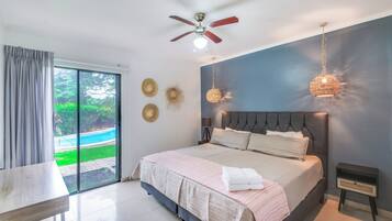 Ein modernes Schlafzimmer mit einem großen Bett, einem Deckenventilator und Blick auf einen Swimmingpool.