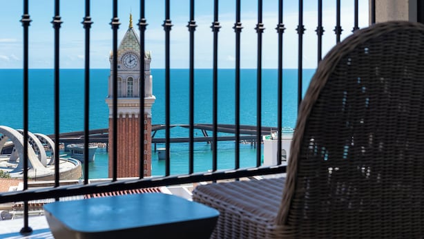 A balcony with a view of the sea, a clock tower, and a bridge. - M Gallery Apartment Phu Quoc (Phu Quoc)