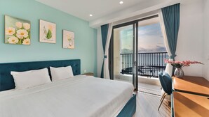 A hotel room with a bed, a desk, and a balcony with a view. - M Gallery Apartment Phu Quoc (Phu Quoc)