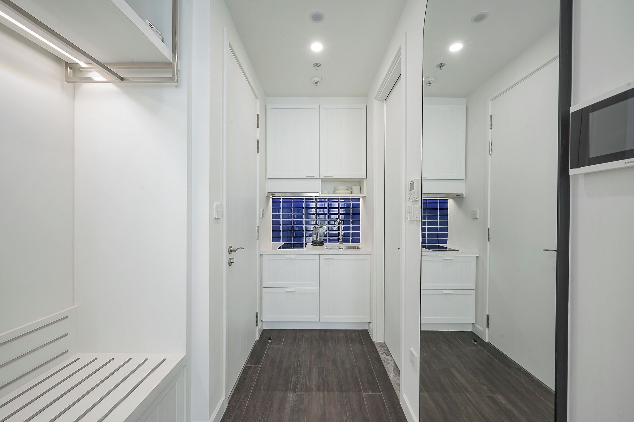A narrow hallway with white cabinets and a blue tiled backsplash in the kitchen area.